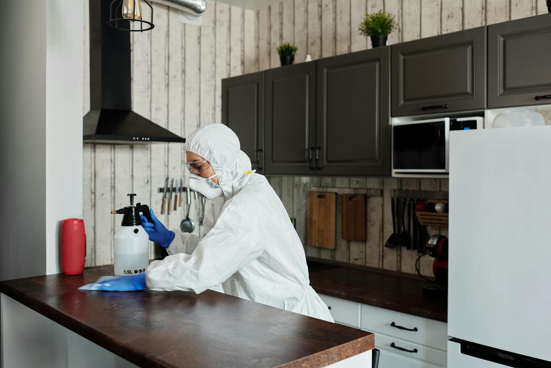 Rooftop Exterminating technician in PPE applying targeted cockroach treatment in a kitchen